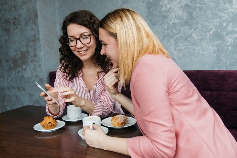 Zwei lächelnde Frauen schauen auf ihr Smartphone, während sie im Café sitzen