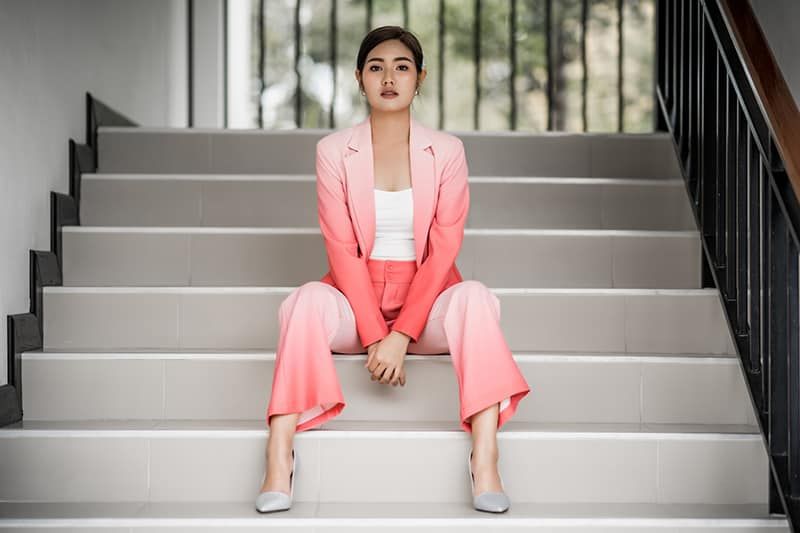 Frau in rosa Blazer und rosa Hose sitzt auf weißen Stufen