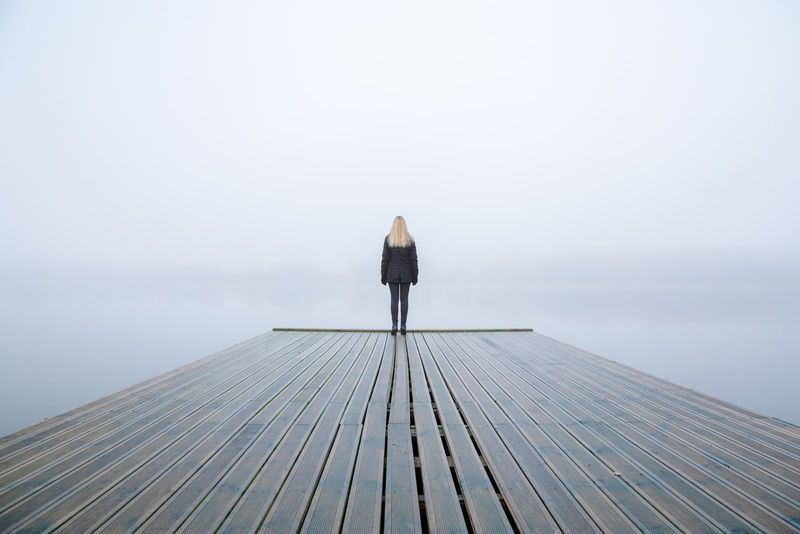 Junge Frau steht allein am Rand einer Fußgängerbrücke und starrt auf den See