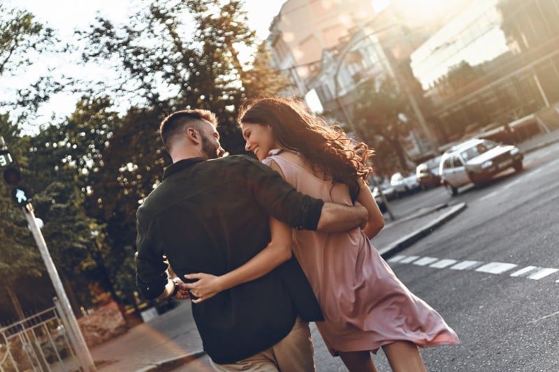 Rückansicht eines Paares, das lächelt und einander ansieht, während es die Straße überquert