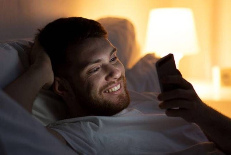 Lächelnder Mann, der nachts auf seinem Telefon tippt
