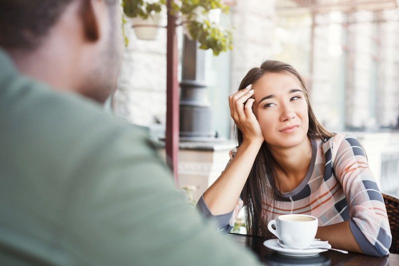 Gelangweilte Frau, die den Mann mit uninteressantem Gesichtsausdruck beim Date in einem Café ansieht