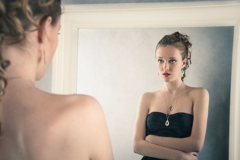 Traurige Frau, die im schwarzen Kleid in den Spiegel schaut