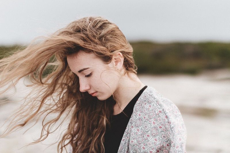 Seitenansicht einer jungen, nachdenklichen, traurigen Frau mit vom Wind verwehten Haaren, die im Freien spaziert
