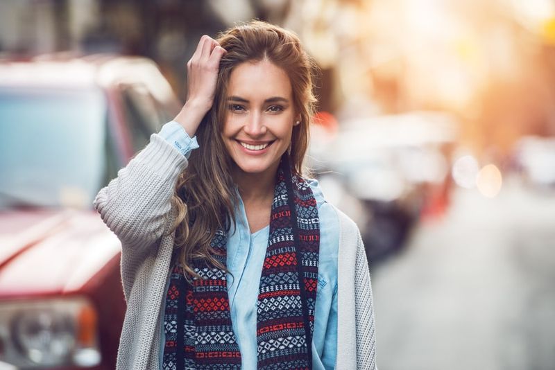 Eine Frau mit langen braunen Haaren geht lächelnd die Straße entlang
