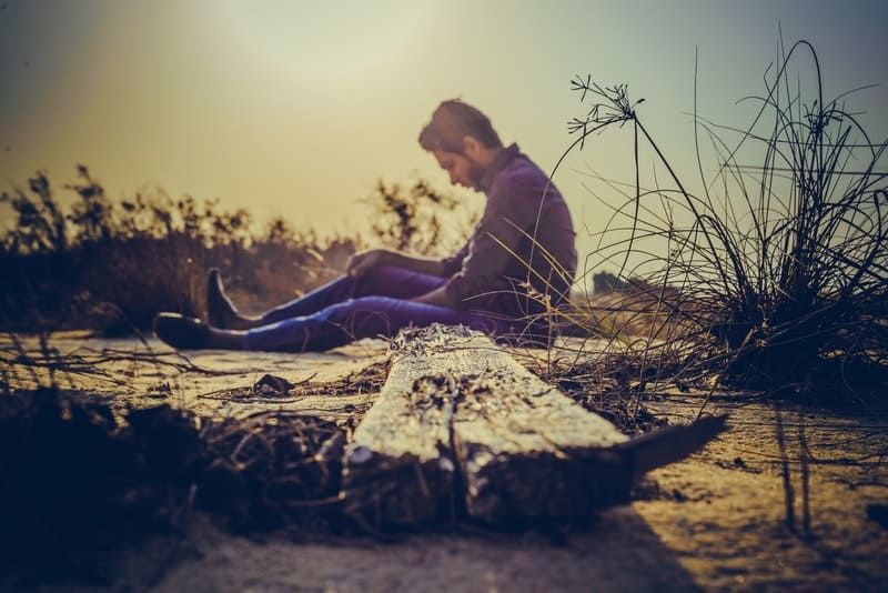 Mann sitzt auf braunem Holzbrett auf dem Boden