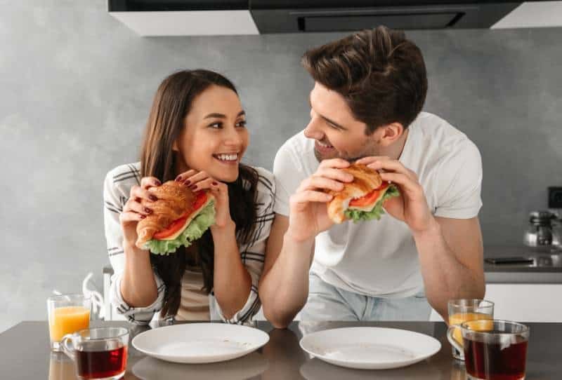 Ein Paar sieht sich an und lächelt, während es Sandwiches isst
