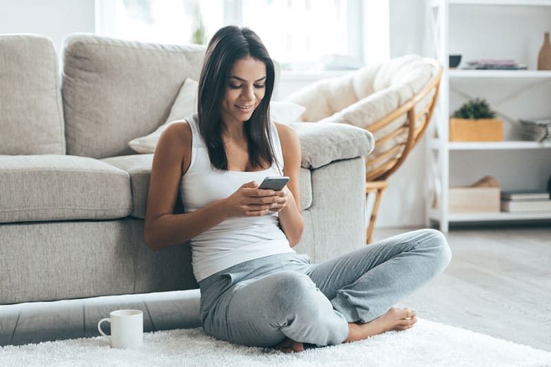 Junge Frau sitzt auf dem Boden und schreibt SMS