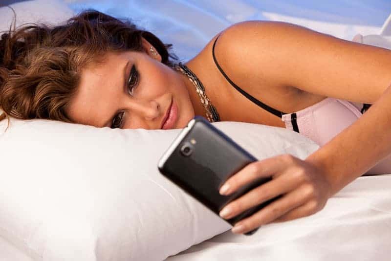 Frau liegt auf dem Bett und tippt auf ihrem Telefon