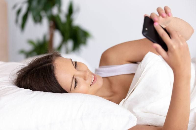 Lächelnde Frau hält Telefon im Bett
