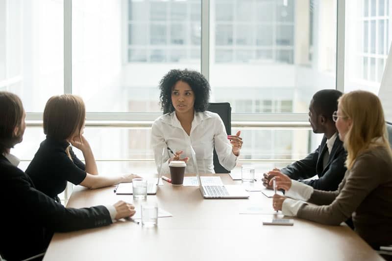 Schwarze Chefin, die ein gemischtrassiges Team-Meeting von Unternehmen leitet, das mit verschiedenen Geschäftsleuten spricht, eine afroamerikanische Führungskraft, die den Projektplan bei einer multiethnischen Gruppenbesprechung im Sitzungssaal bespricht