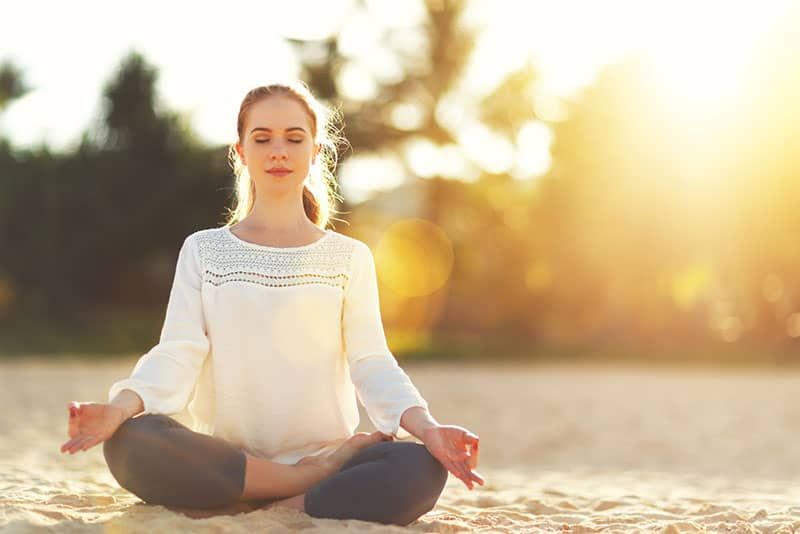 Frau praktiziert Yoga und meditiert im Lotussitz am Strand