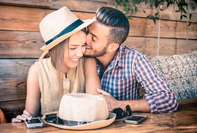 Mann küsst lächelnde Frau im Café auf die Wange