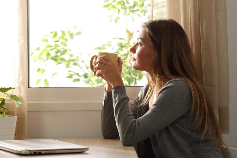 eine imaginäre Frau, die sitzt und aus dem Fenster schaut, während sie Kaffee trinkt