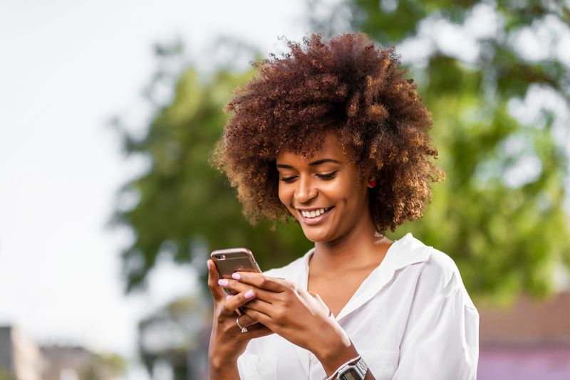 Lächelnde Frau mit lockigem Haar, die im Freien SMS schreibt