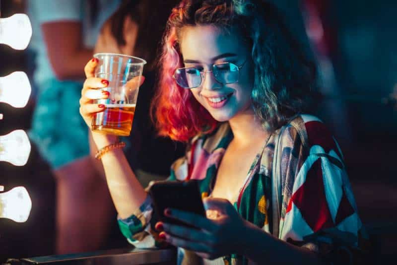 Junge Frau trinkt Bier und tippt auf ihrem Smartphone