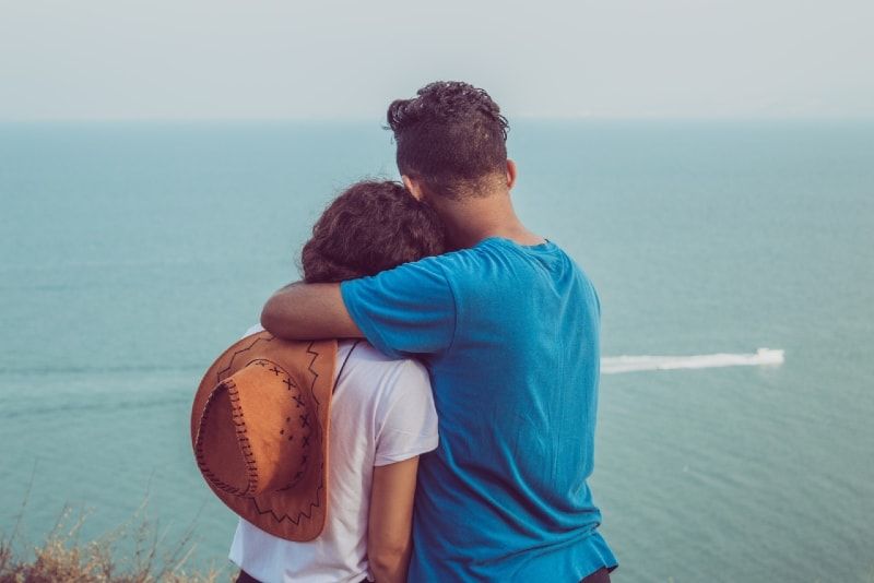 Mann umarmt Frau beim Blick aufs Meer