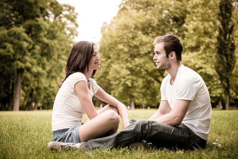 Mann und Frau unterhalten sich, während sie auf Gras sitzen