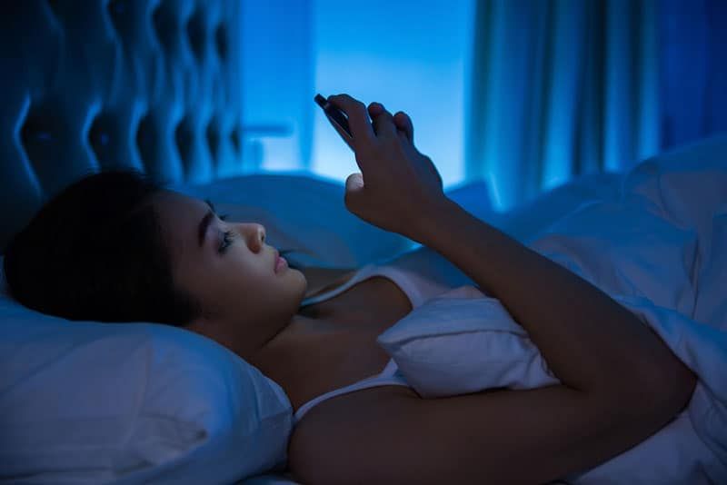 Frau tippt auf ihrem Telefon, während sie nachts im Bett liegt