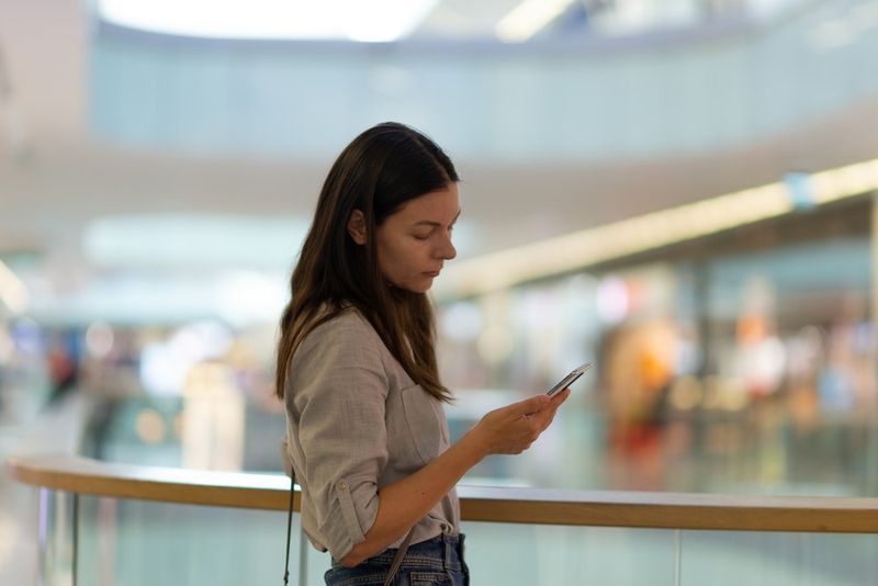 Eine traurige Brünette in einem Einkaufszentrum benutzt ein Smartphone