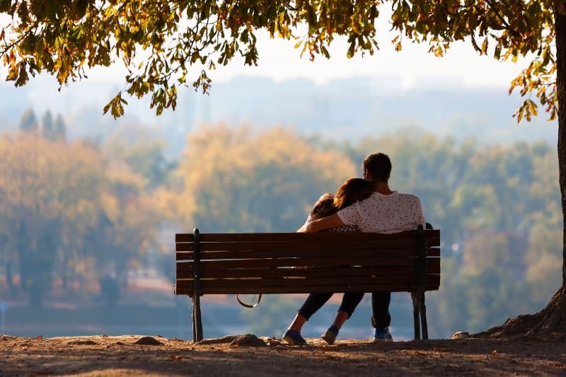 Rückansicht eines Mannes, der ihre Frau auf einer Parkbank umarmt