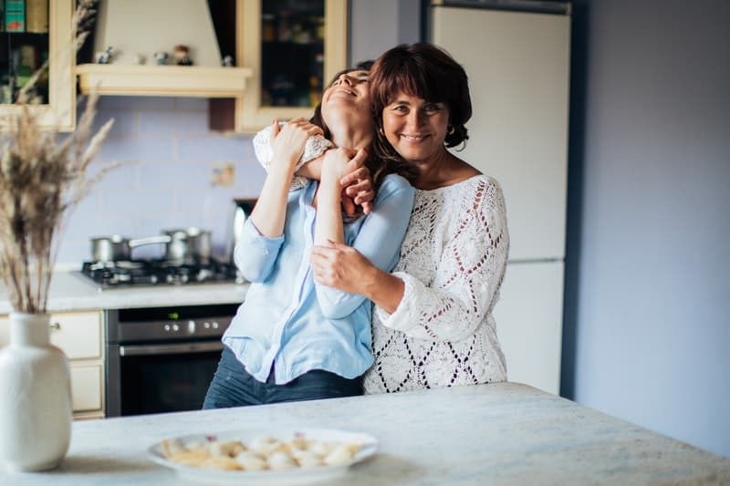 Frau wird von einer älteren Frau umarmt, während sie in der Küche steht