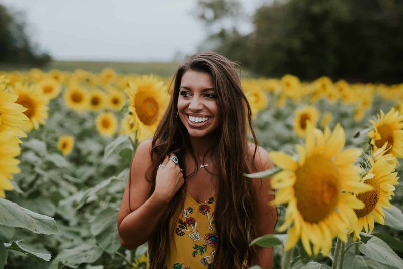 Glückliche Frau im gelben Kleid, die im Sonnenblumenfeld steht