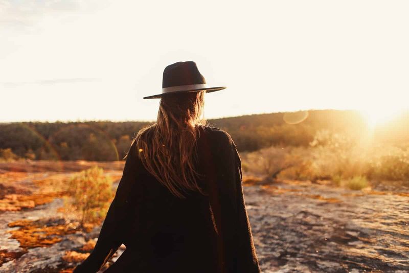 Frau mit Hut steht bei Sonnenuntergang auf Felsen