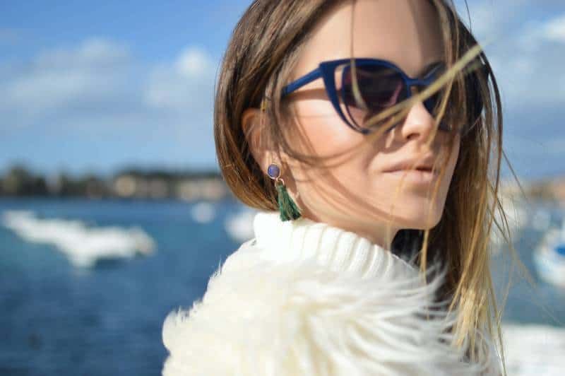 Frau trägt blau gerahmte Cat-Eye-Sonnenbrille mit Wasser im Hintergrund