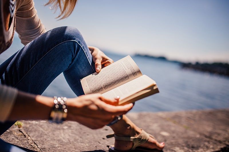 Frau liest ein Buch, während sie neben einem Gewässer sitzt