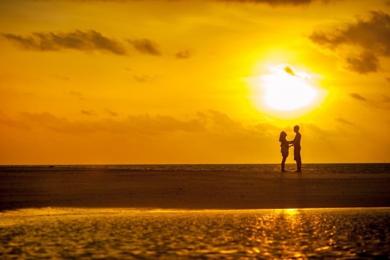 Mann und Frau stehen bei Sonnenuntergang am Meeresufer