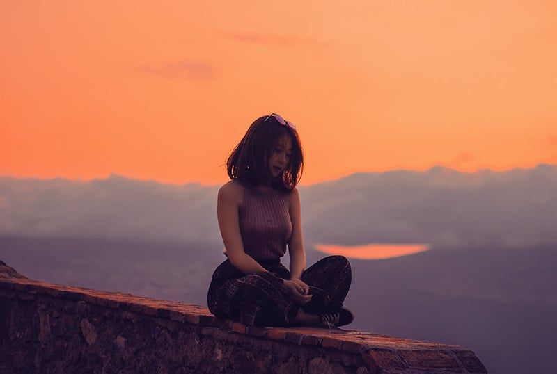 Frau sitzt bei Sonnenuntergang auf einer Klippe