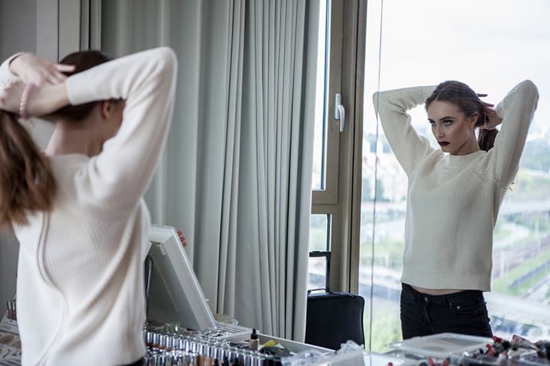 Frau im weißen Pullover steht vor dem Spiegel