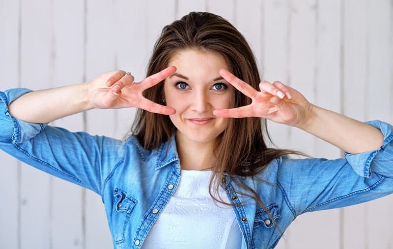 Frau zeigt Handzeichen von zwei Friedenszeichen in der Nähe ihrer Augen