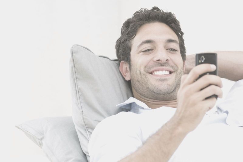 grinsender Mann, der sich hinlegt, während er eine Nachricht von seinem Handy liest