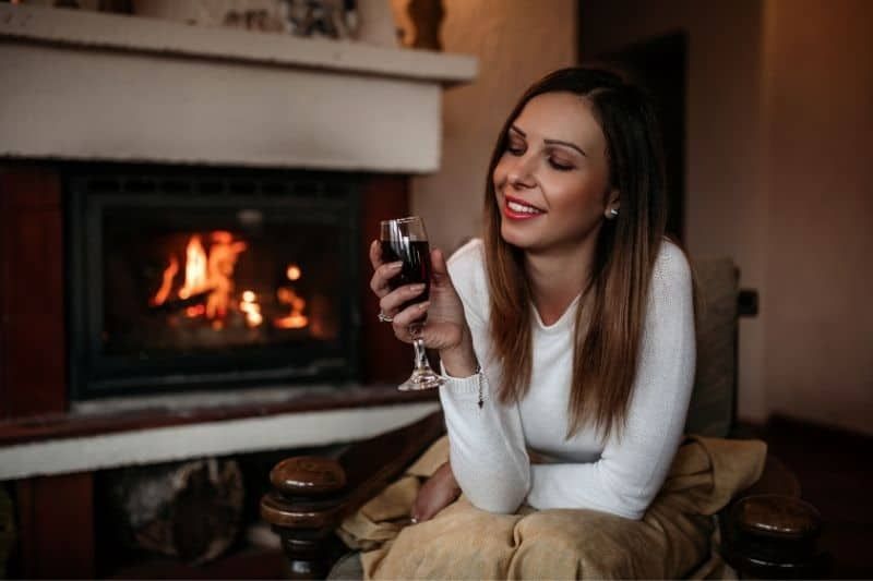 Frau genießt es allein im Haus mit Wein am Kamin