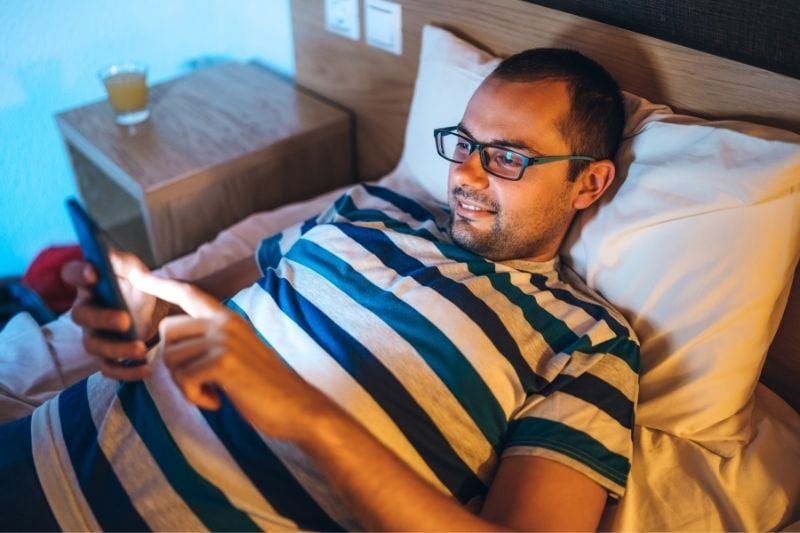 Mann liest Nachrichten von seinem Smartphone, während er im Bett liegt