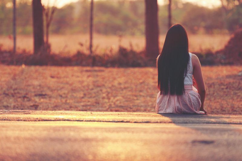 Frau mit langen Haaren sitzt allein im Freien