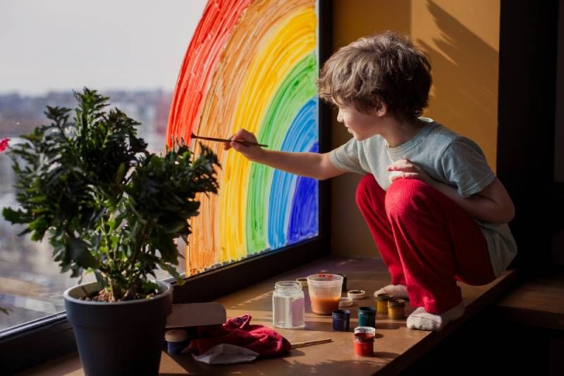 Kind zeichnet Regenbogen auf Fenster