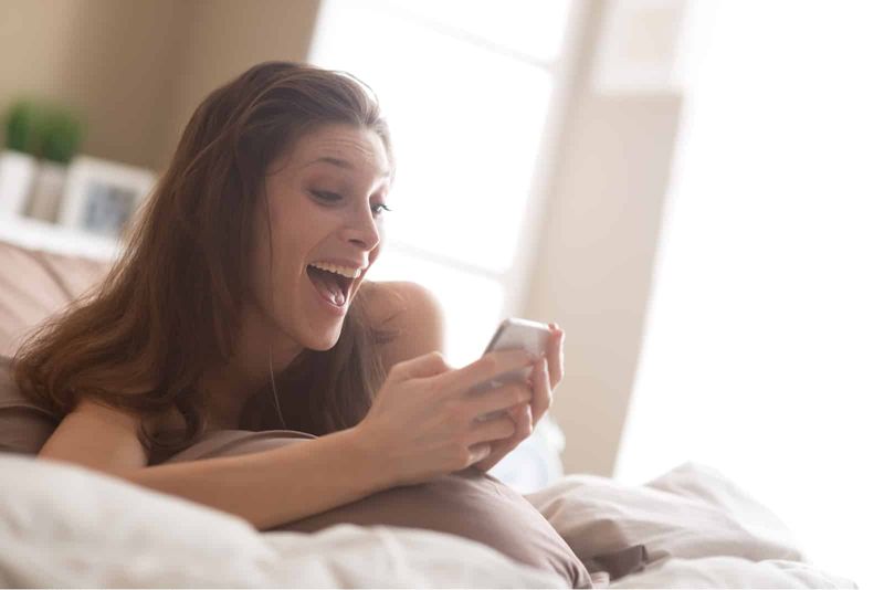 Frau liegt mit Telefon in der Hand auf ihrem Bett