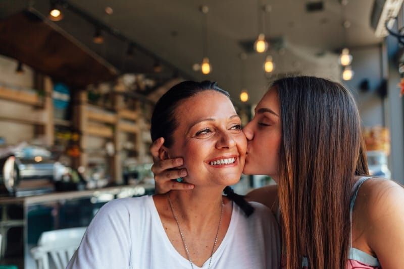 Tochter küsst Mutter, während sie im Café sitzt