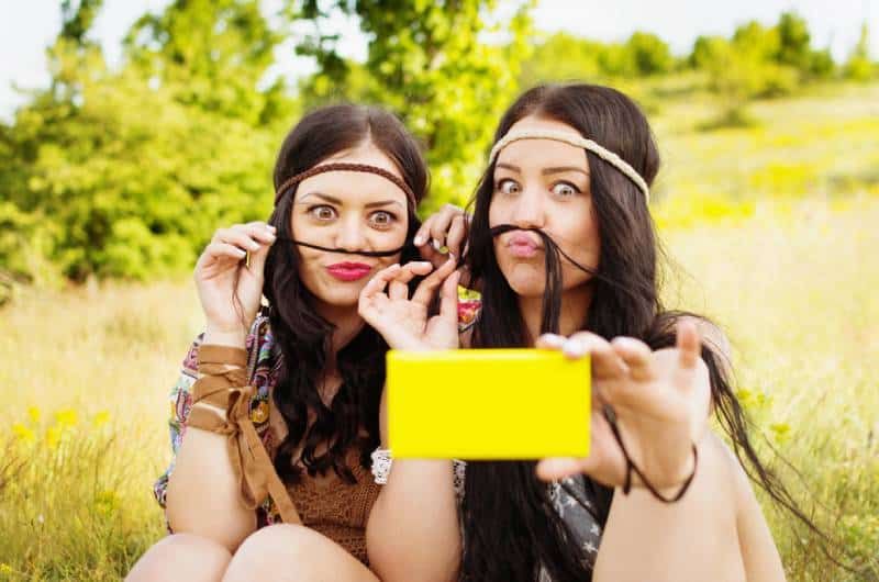 Boho-Mädchen mit langen Haaren, die Schnurrbart machen und ein Selfie im Park machen