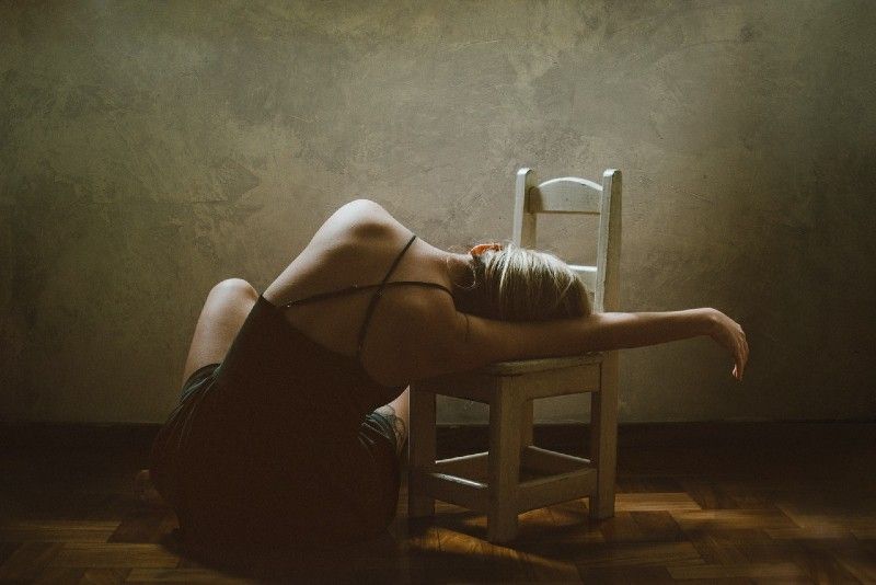 Frau sitzt auf dem Boden und stützt sich auf einen Stuhl