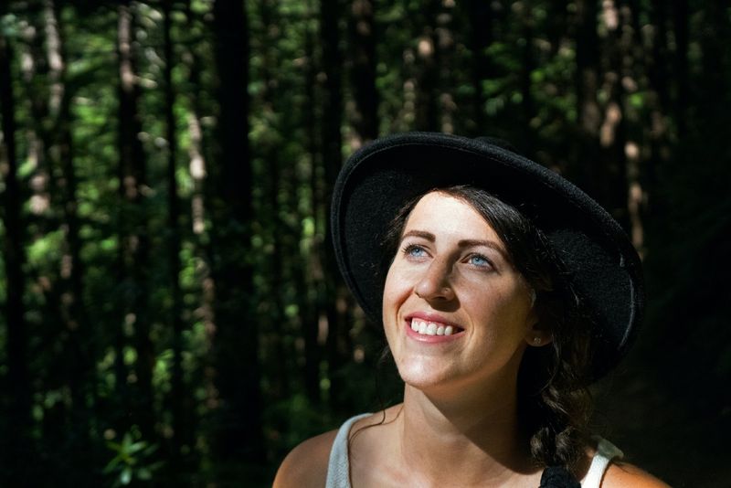 Frau mit schwarzem Hut lächelt im Wald