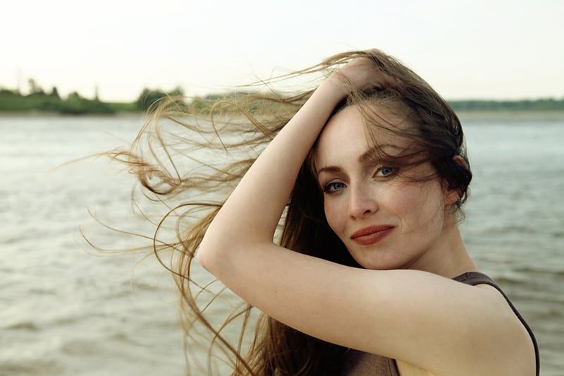 Frau berührt ihr Haar, während sie in der Nähe des Gewässers steht