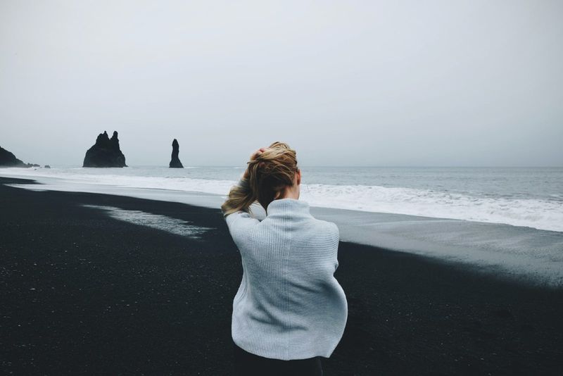 Frau im grauen Pullover sitzt am Strand