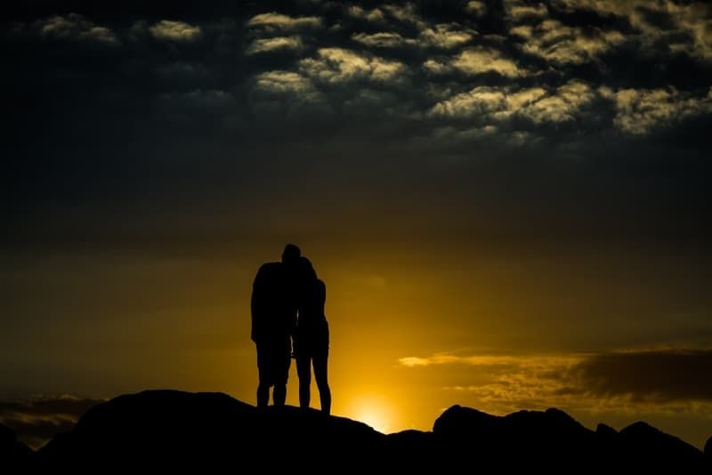 Mann und Frau stehen bei Sonnenuntergang auf einem Hügel
