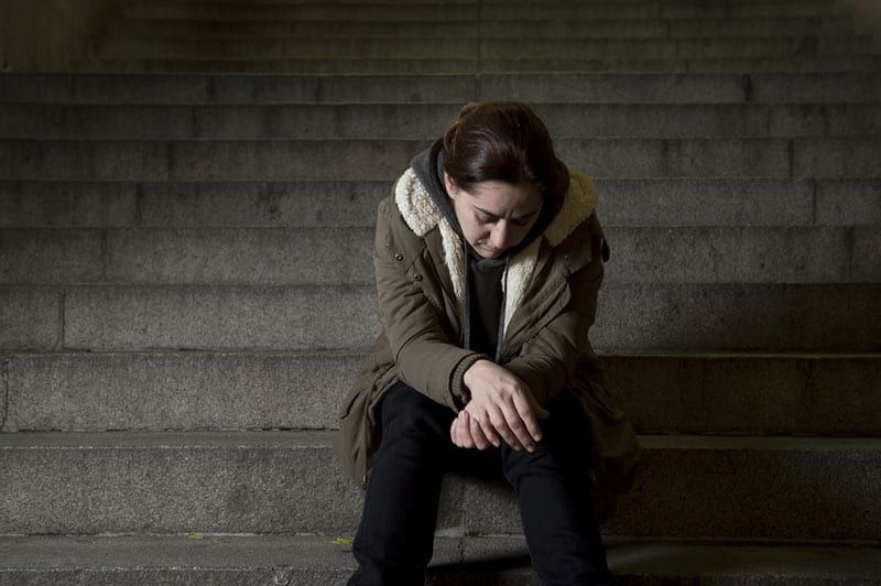 Traurige Frau allein auf der U-Bahn-Treppe auf der Straße, die unter Depressionen leidet und krank und hilflos aussieht und einsam als weibliches Missbrauchsopfer im dunklen städtischen Nacht-Grunge-Hintergrund sitzt