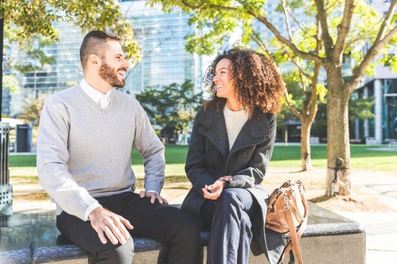 Geschäftsfrau und Mann reden und sitzen draußen auf der Bank