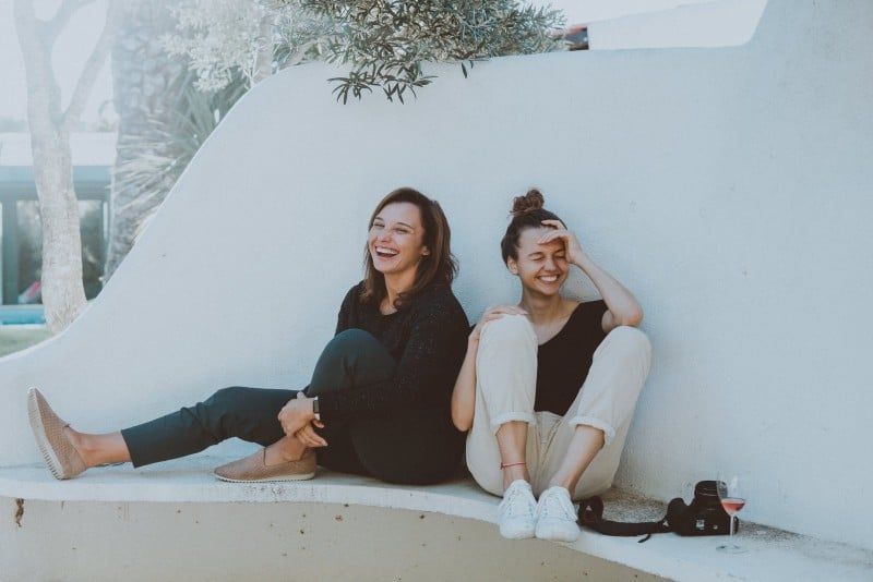 Zwei Frauen sitzen auf einer weißen Bank und lächeln